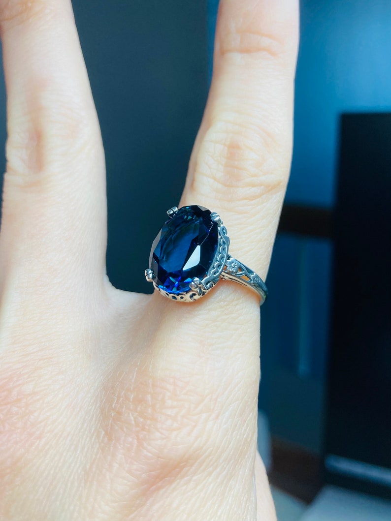 May include: A silver ring with a large, oval-shaped, dark blue gemstone set in a decorative, filigree-style band.