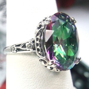 May include: A silver ring with a large, oval-shaped, iridescent gemstone. The gemstone is a mix of green, purple, and blue colors. The ring has a detailed, ornate design.