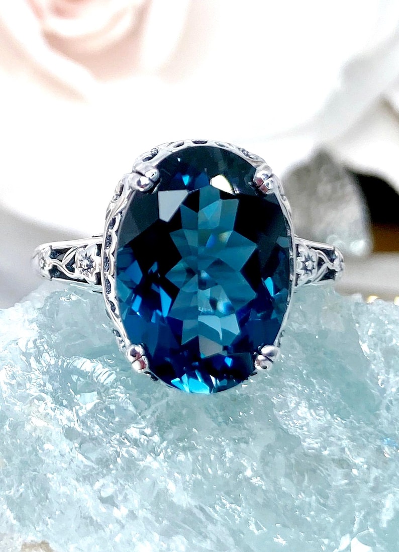 May include: A silver ring with a large, oval-shaped, blue topaz gemstone. The ring has a delicate, ornate design with floral accents.