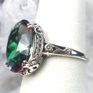 May include: A silver ring with a large, oval-shaped, green gemstone with rainbow iridescent facets. The ring has a filigree design with floral accents.