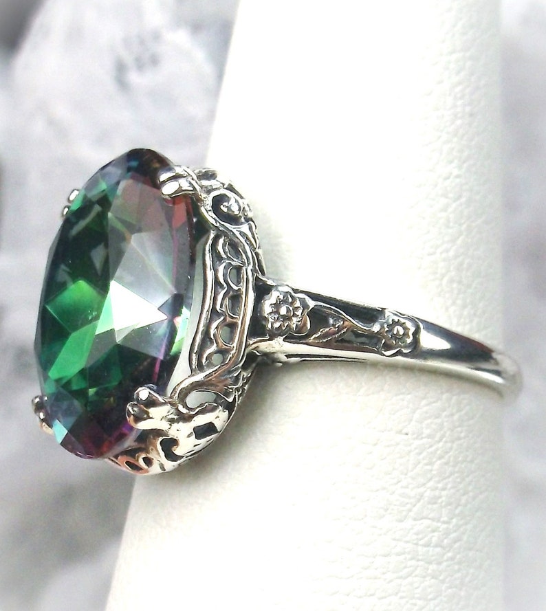 May include: A silver ring with a large, oval-shaped, green gemstone with rainbow iridescent facets. The ring has a filigree design with floral accents.