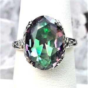 May include: A silver ring with a large oval-shaped iridescent gemstone. The gemstone is a deep green color with flashes of purple and blue.