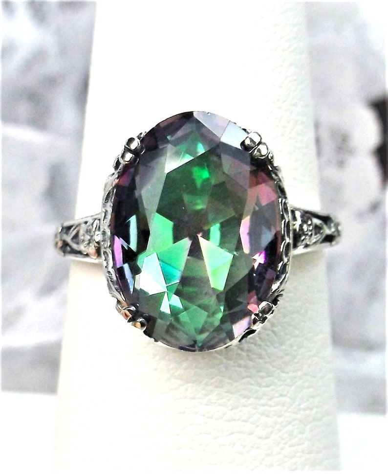 May include: A silver ring with a large oval-shaped iridescent gemstone. The gemstone is a deep green color with flashes of purple and blue.