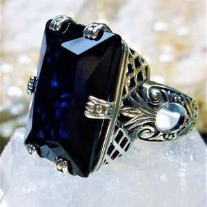 May include: A silver ring with an ornate design features a large, dark blue rectangular gemstone.