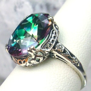 May include: A silver ring with an oval-shaped, iridescent gemstone set in a filigree design. The gemstone has shades of green, blue, purple, and pink.