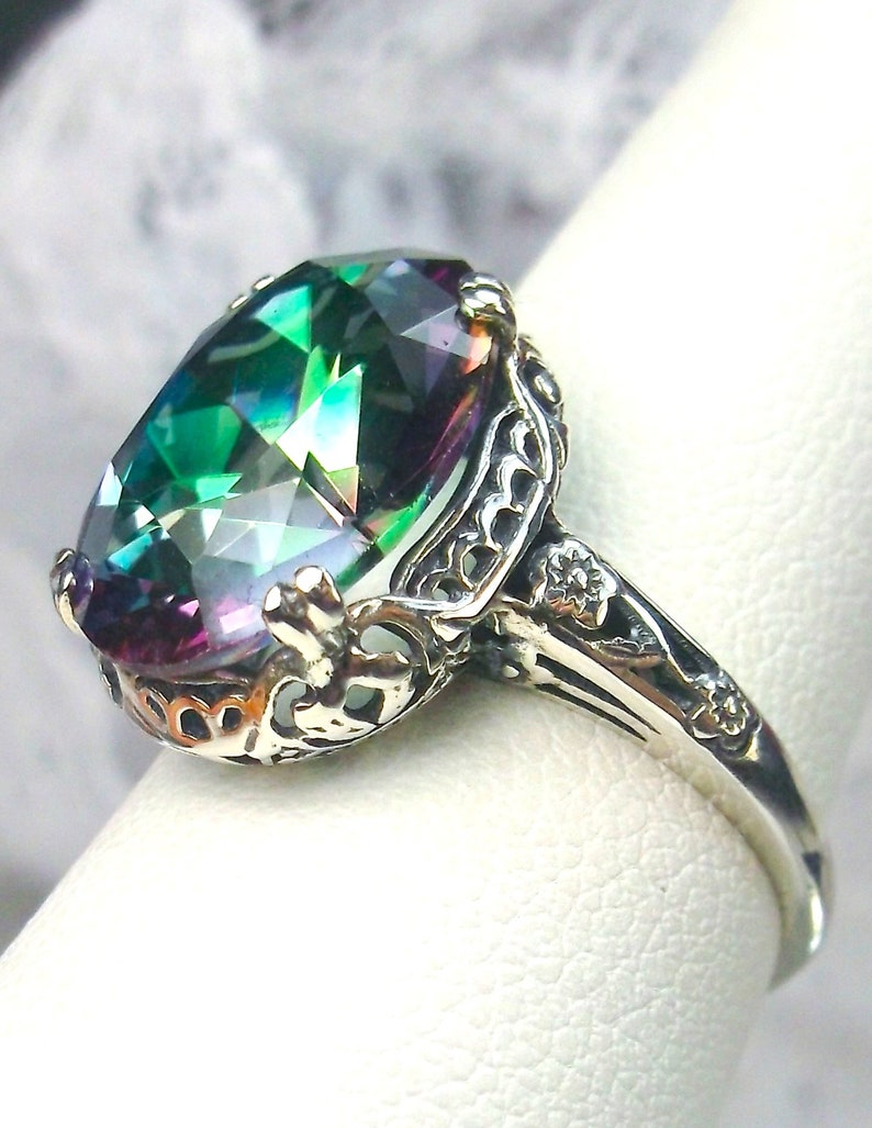May include: A silver ring with an oval-shaped, iridescent gemstone set in a filigree design. The gemstone has shades of green, blue, purple, and pink.