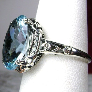 May include: A silver ring with a large, oval-shaped blue topaz gemstone set in a filigree design. The ring has a delicate, intricate band with small accents.