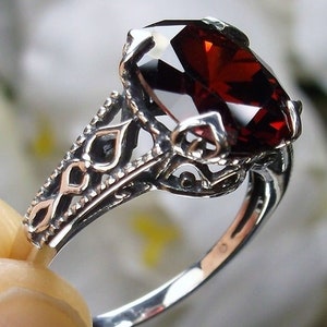 May include: A silver ring with an ornate filigree design and a large, dark red gemstone.