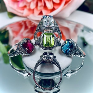 May include: Four silver rings with different colored gemstones. The rings are stacked on top of each other. The gemstones are red, green, blue, and clear.