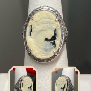May include: A silver ring with a white cameo featuring a woman's profile. The cameo is set in a filigree design.