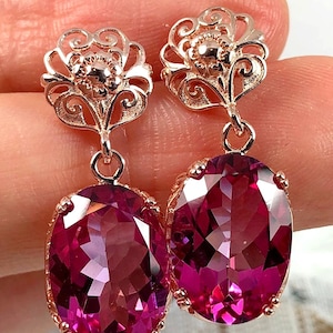 May include: A pair of rose gold earrings with pink oval-shaped gemstones. The earrings feature a delicate filigree design.