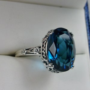 May include: A silver ring with a large, oval-shaped, dark blue gemstone set in a filigree design.