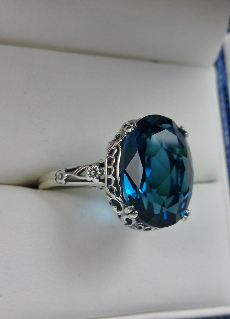 May include: A silver ring with a large, oval-shaped, dark blue gemstone set in a filigree design.