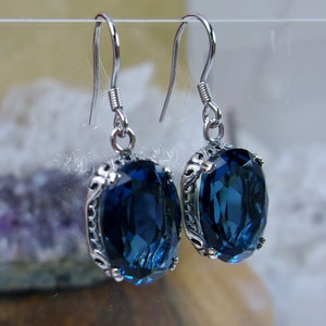 May include: A pair of silver earrings with a dark blue oval-shaped gemstone set in a silver filigree design.