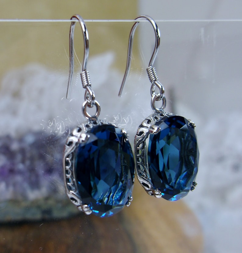 May include: A pair of silver earrings with a dark blue oval-shaped gemstone set in a silver filigree design.