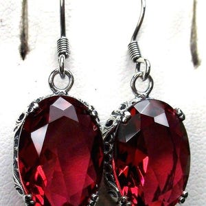 May include: A pair of silver earrings with red gemstone drops. The earrings have a delicate, ornate design and feature oval-shaped gemstones.