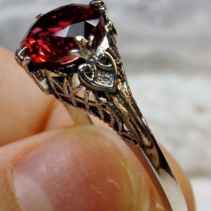 Pode incluir: Um anel de prata com um delicado design de filigrana apresenta uma grande pedra vermelha de forma oval.