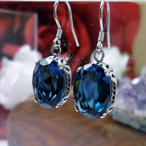 May include: A pair of silver earrings with a dark blue oval-shaped gemstone set in a silver filigree design.