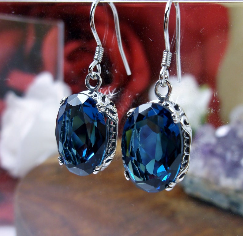 May include: A pair of silver earrings with a dark blue oval-shaped gemstone set in a silver filigree design.