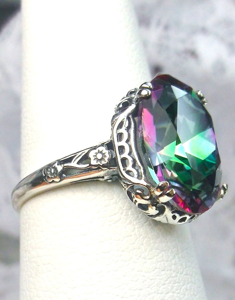 May include: A silver ring with an oval-shaped, multi-colored gemstone set in a filigree design.