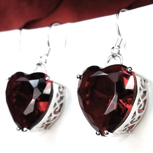 Puede incluir: Un par de pendientes de plata en forma de corazón con grandes piedras preciosas facetadas rojas.