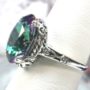 May include: A silver ring with an oval-shaped, iridescent gemstone set in a filigree design. The gemstone has shades of green, blue, and purple.