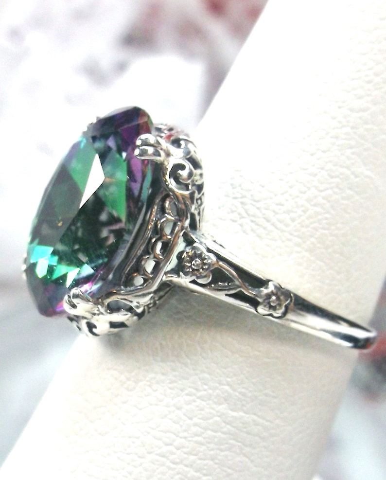 May include: A silver ring with an oval-shaped, iridescent gemstone set in a filigree design. The gemstone has shades of green, blue, and purple.
