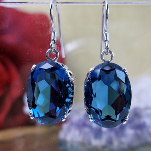 May include: A pair of silver dangle earrings with large oval-shaped blue gemstones. The gemstones are faceted and have a deep blue color.