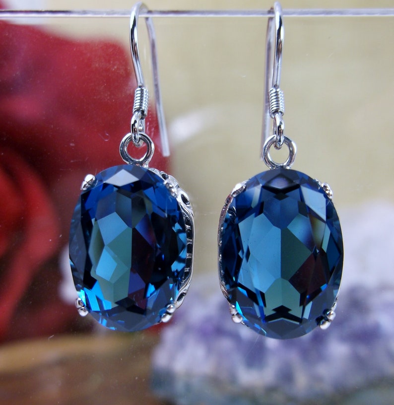 May include: A pair of silver dangle earrings with large oval-shaped blue gemstones. The gemstones are faceted and have a deep blue color.