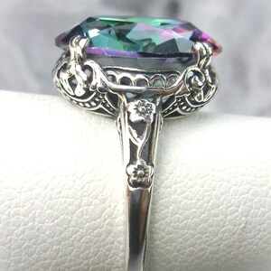 May include: A silver ring with an ornate design features a large, oval-shaped, iridescent gemstone with shades of green, blue, and purple.