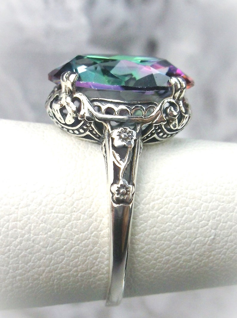 May include: A silver ring with an ornate design features a large, oval-shaped, iridescent gemstone with shades of green, blue, and purple.