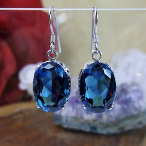 May include: A pair of silver dangle earrings with large oval-shaped blue gemstones. The earrings have a simple design and are perfect for everyday wear.