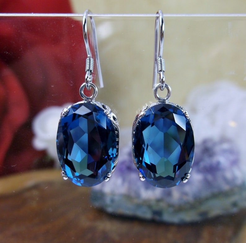 May include: A pair of silver dangle earrings with large oval-shaped blue gemstones. The earrings have a simple design and are perfect for everyday wear.