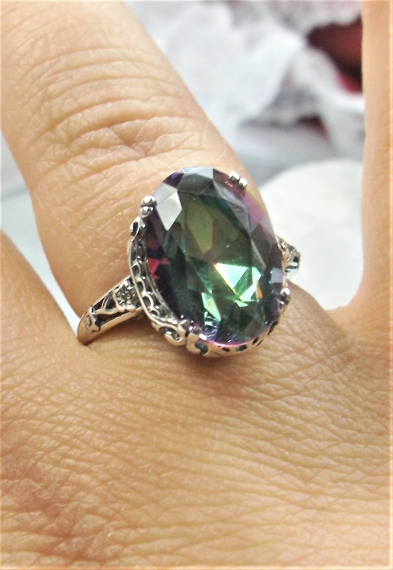 May include: A silver ring with an oval-shaped, iridescent gemstone. The gemstone has shades of green, blue, and purple.