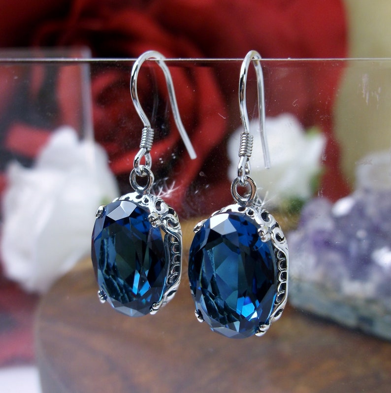 May include: A pair of silver dangle earrings with a large oval blue gemstone. The earrings have a delicate filigree design.