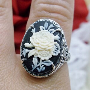 May include: A silver ring with a black cameo featuring a white carved flower design.