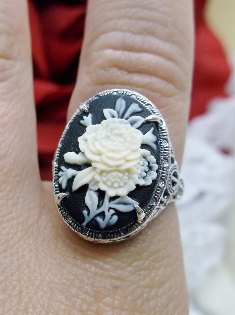 May include: A silver ring with a black cameo featuring a white carved flower design.