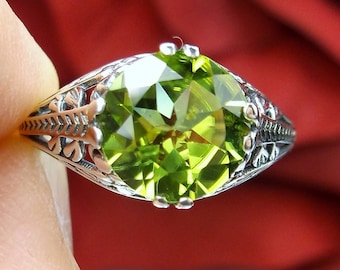 May include: A silver ring with an ornate design features a large, faceted, green gemstone.