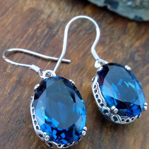 May include: A pair of silver earrings with blue gemstone oval drops. The earrings have a delicate filigree design around the stones.