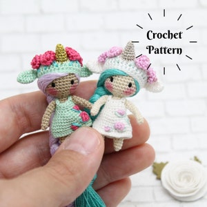 Puede incluir: Dos muñecas de unicornio de crochet con diademas florales y pelo largo de hilo. Las muñecas llevan vestidos con detalles florales. Las muñecas están sujetas en una mano. Patrón de crochet.