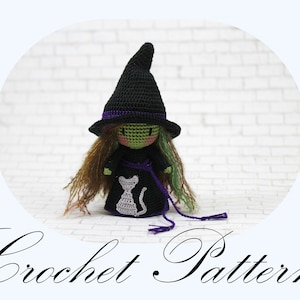 Puede incluir: Muñeca de bruja de ganchillo con sombrero y vestido negros, piel verde y pelo largo castaño y verde. El vestido presenta un diseño de gato blanco. El texto "Crochet Pattern" está en la parte inferior.