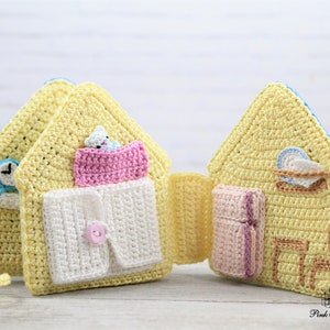 May include: A yellow crocheted house-shaped toy with different rooms that open up to reveal a bed, a shirt, a clock, a plate, and a chair. The toy is made with soft yarn and is perfect for imaginative play.