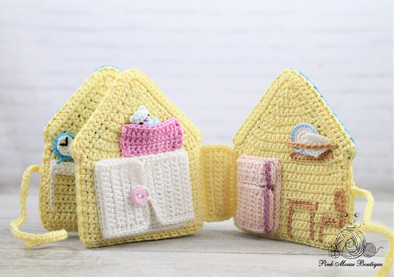 May include: A yellow crocheted house-shaped toy with different rooms that open up to reveal a bed, a shirt, a clock, a plate, and a chair. The toy is made with soft yarn and is perfect for imaginative play.
