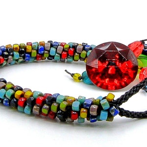 May include: A colourful beaded bracelet with a large red faceted bead and a black cord closure. The bracelet is approximately the size of a UK penny.