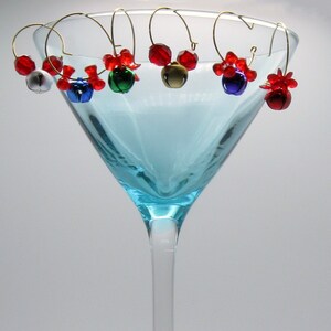 May include: A set of six blue, red, and green jingle bell wine glass charms. The charms are attached to a gold wire and have a red bead at the top.