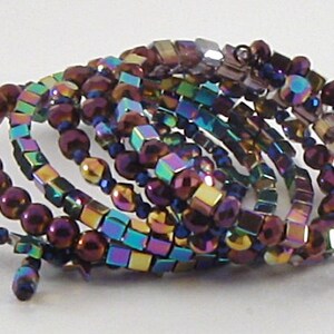 May include: A multi-strand bracelet made of iridescent, faceted beads in shades of purple, blue, and gold. The beads are arranged in a spiral pattern.