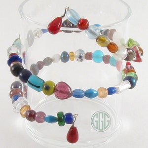 May include: A colorful beaded bracelet with a heart-shaped bead and a red glass pendant. The bracelet is wrapped around a clear glass container.