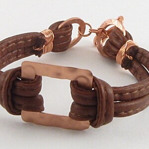 May include: A brown leather bracelet with a copper square accent and a copper clasp.