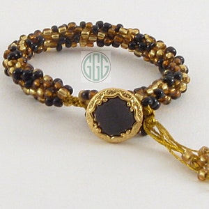 May include: A black and gold beaded bracelet with a black stone button closure and a gold tassel.