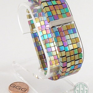 May include: A multi-colored iridescent bracelet made of small square beads. The bracelet is on a clear display stand. The bracelet has a silver clasp.